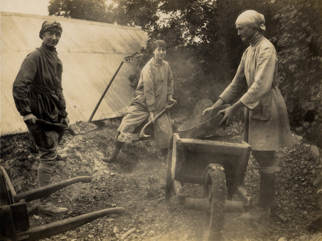 women in more practical clothes with hoes and scythes