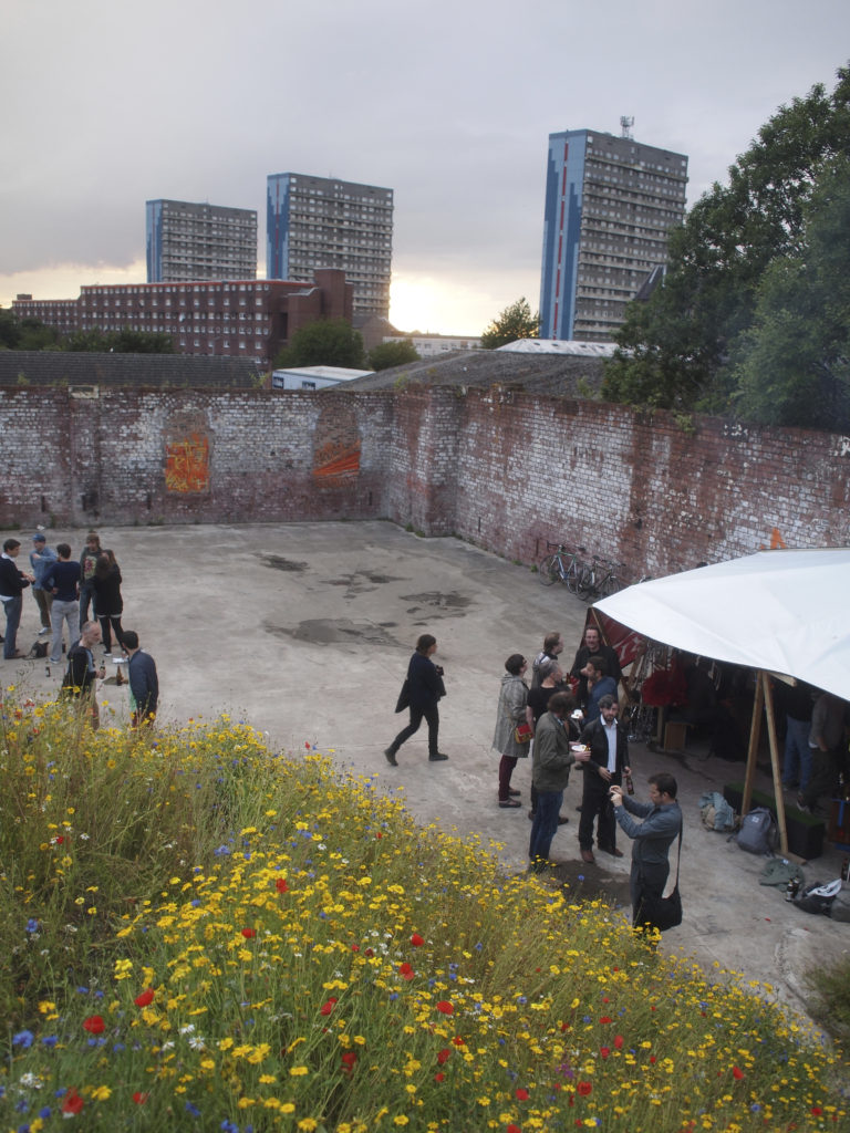 A group of young people discussing plans in a walled space, behind the skyline is dominated by high rise flats 