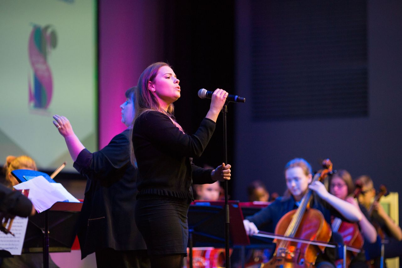 A young woman sings at the mic, supported by strings of the City of Edinburgh Music School