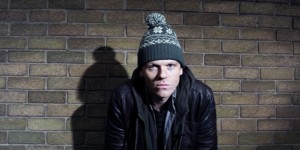 Loki in bobble hat and hunched shoulders against a wall
