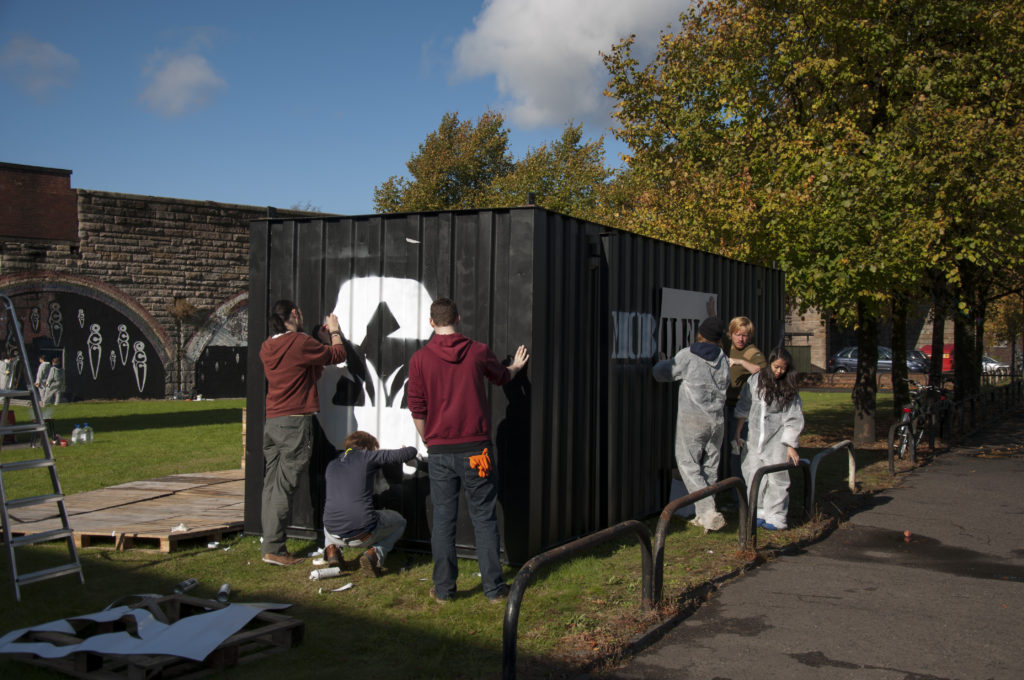 Mobileland, eco-design project, part of Stalled Spaces, students painting containers in walled space 