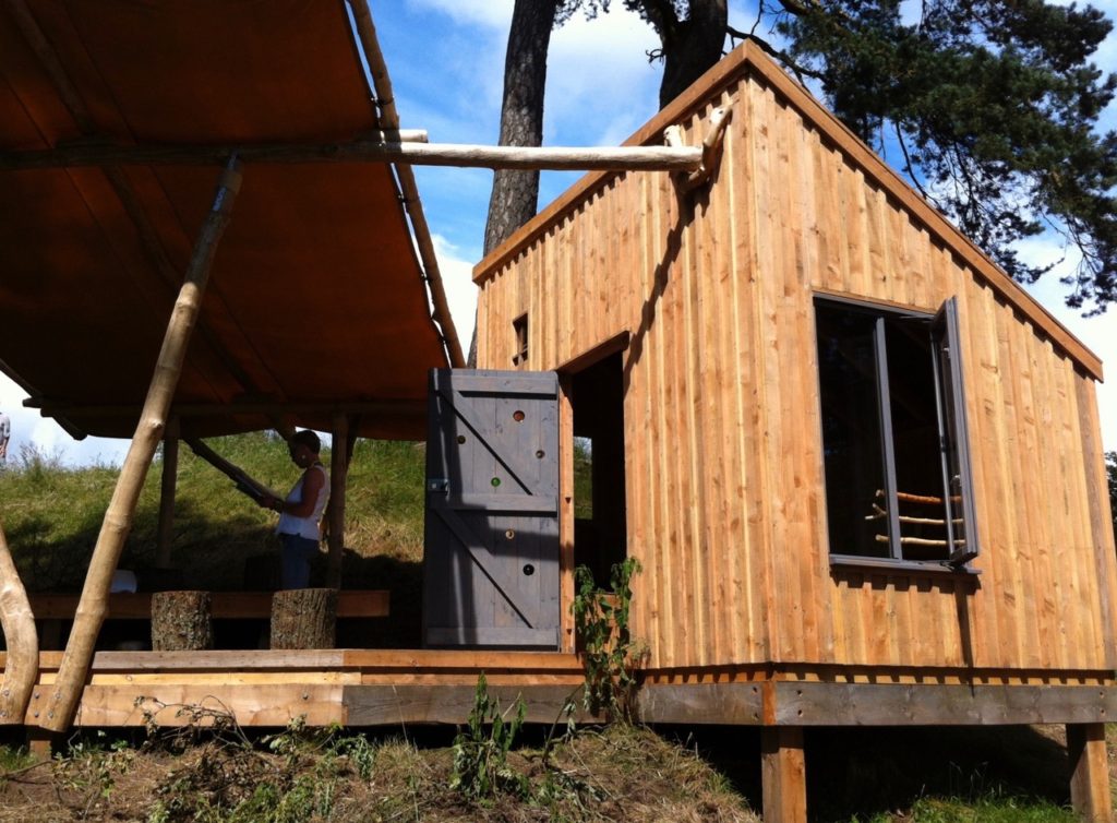 A woman stands on a veranda in front of a wooden hut: image by Ray Perman