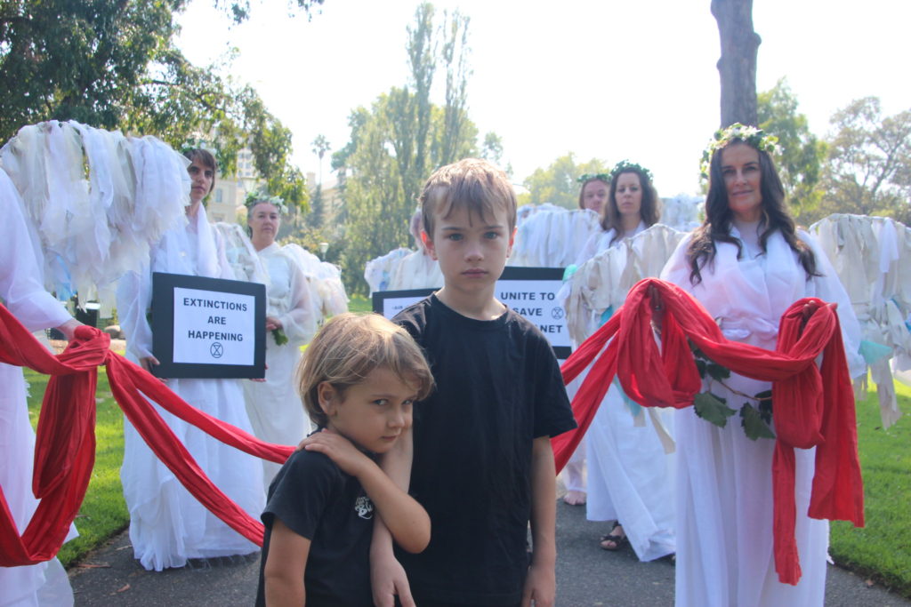 Two young children stare at the camera, surrounded by Climate Angels in white. by Takver at mass demonstration in Melbourne CC BY-SA 2.0
