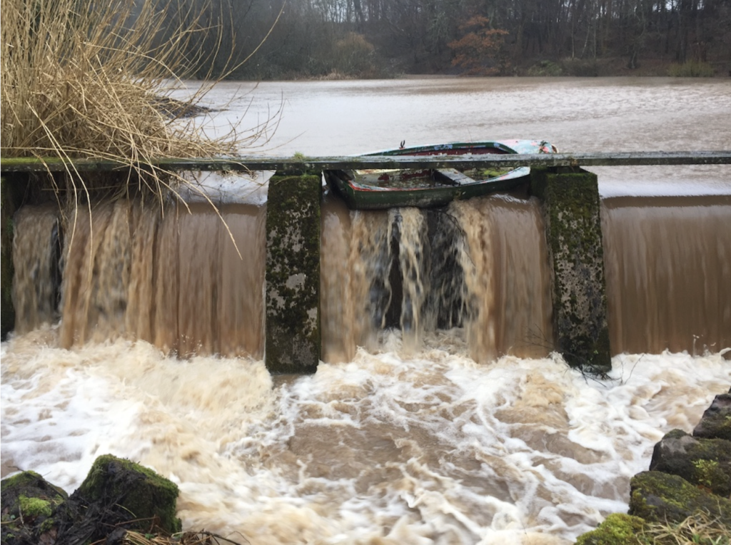 A torrent of water washes an old rowing boat into a sluice during floods in Perth and Kinross 2022