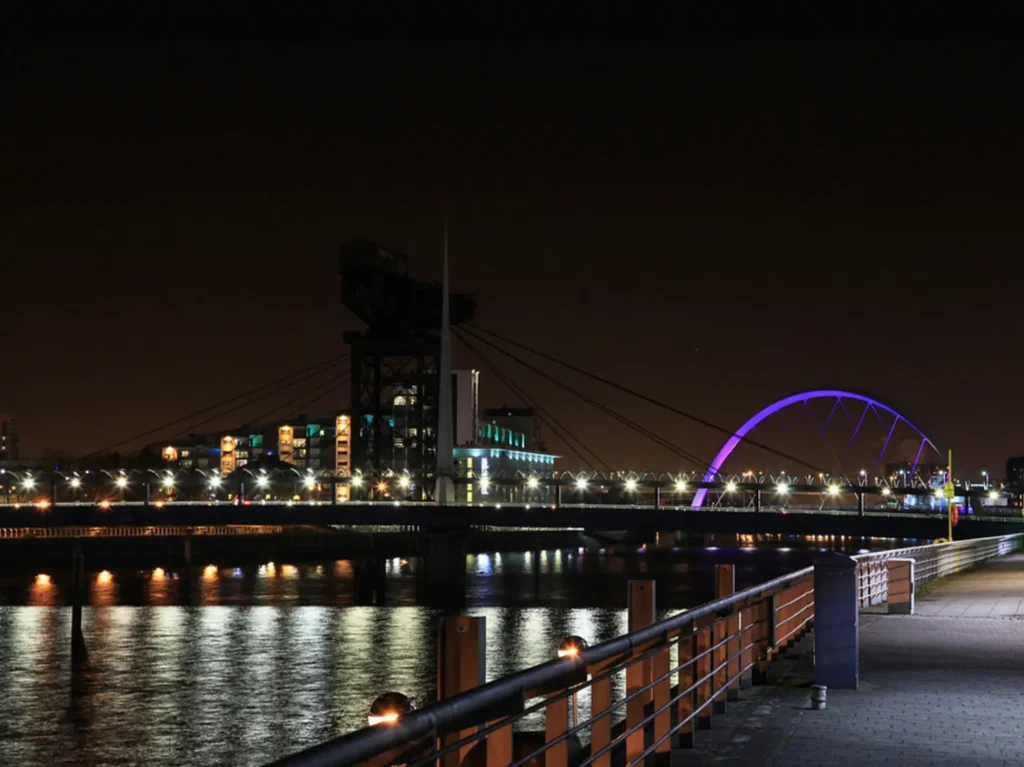 A picture of the Squinty Bridge, Glasgow at night, lights reflected on the dark Clyde